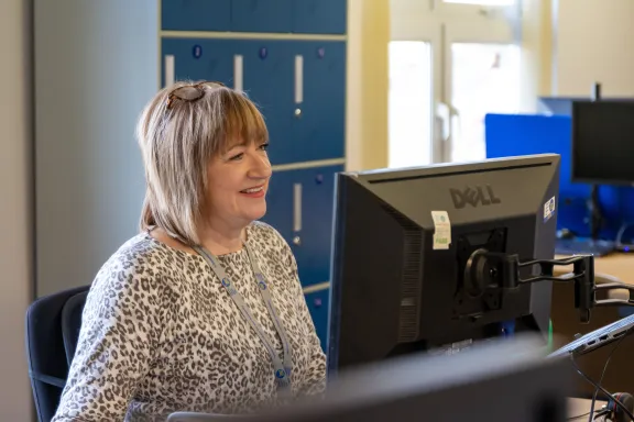 Adviser smiling whilst working on a desktop PC. 
